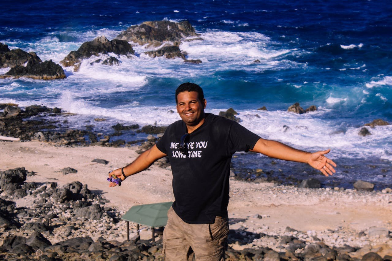 Smiling man on rocky Santa Cruz beach, Aruba, embracing ocean waves.